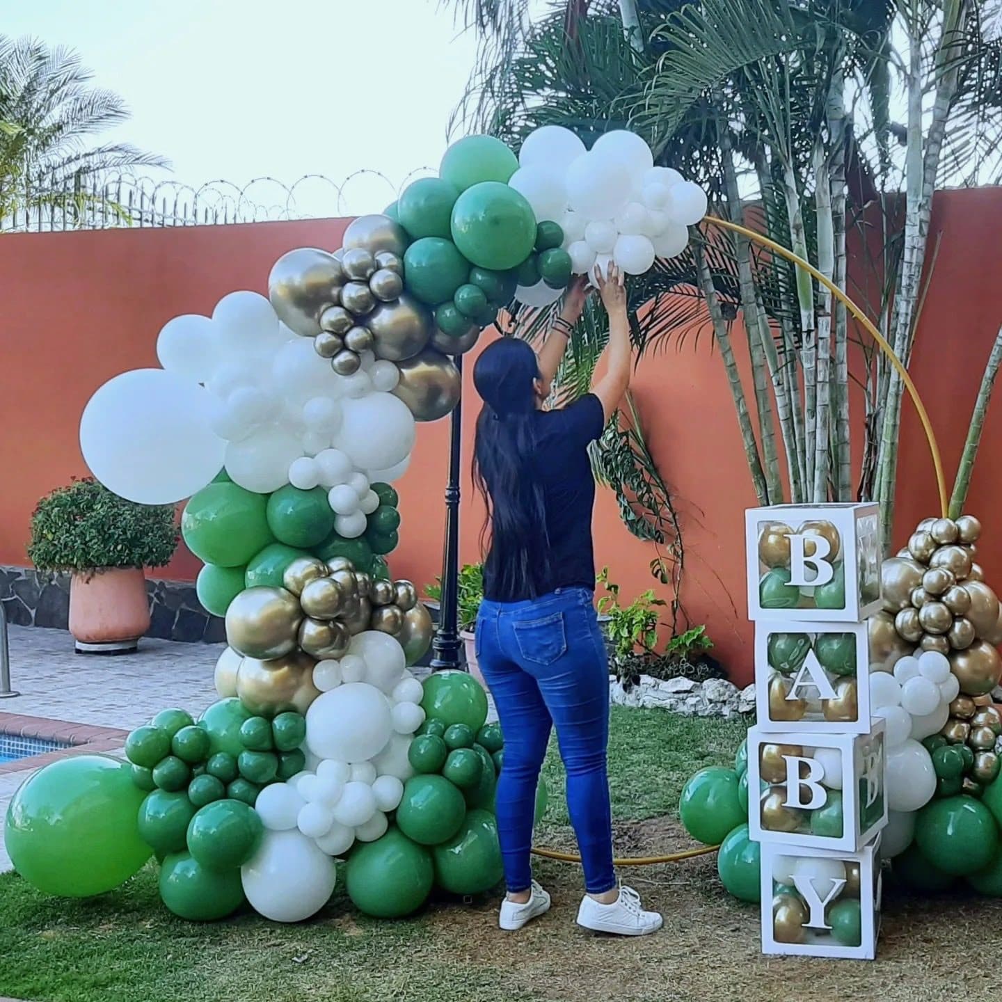 Green, white and gold organic balloon arch outdoors with wooden blocks spelling BABY