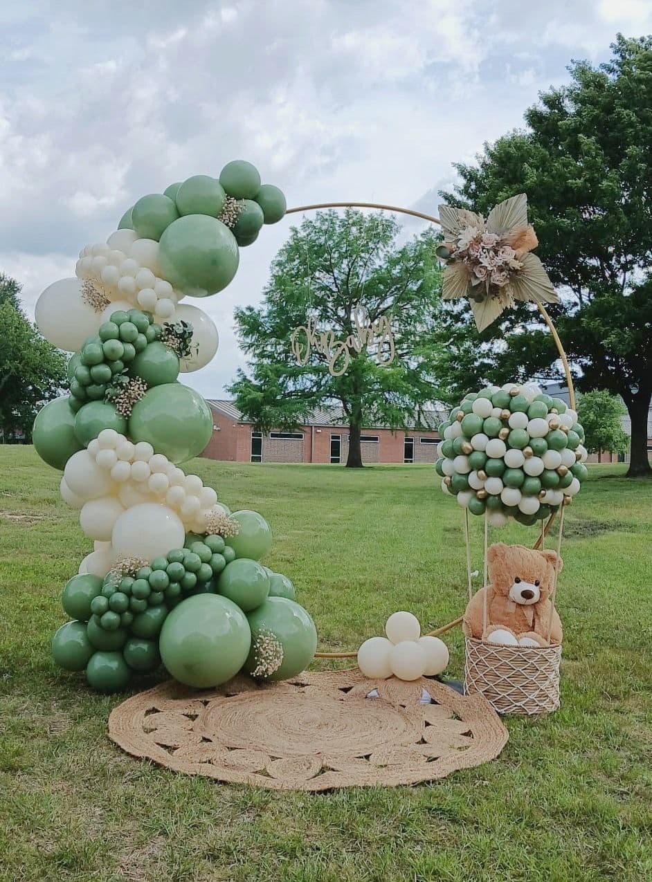 Sage green and cream balloon hoop arch with a teddy bear in a basket at an outdoor baby shower