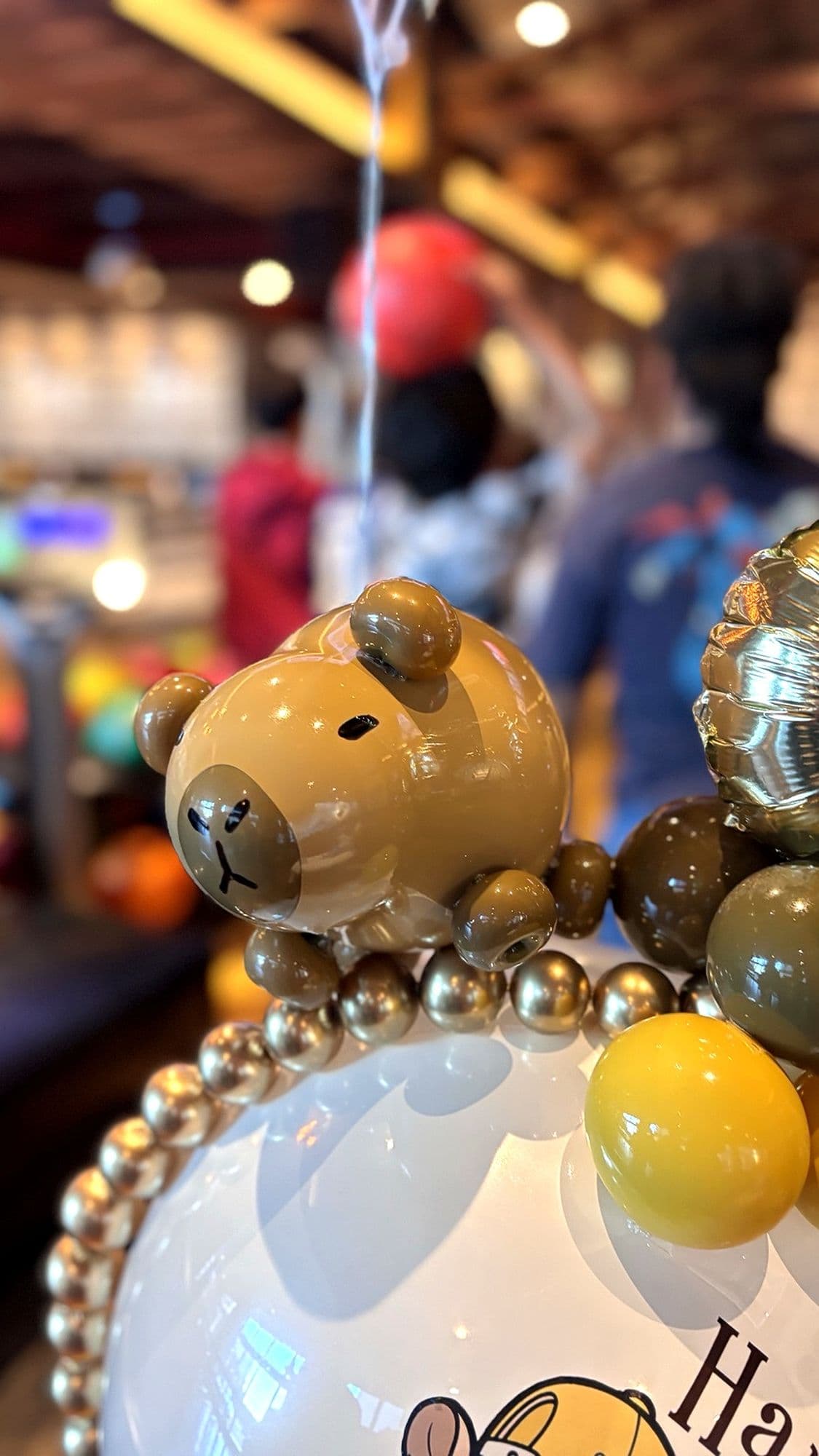 Close-up of a bear-themed bubble balloon with gold pearls on a birthday balloon bouquet