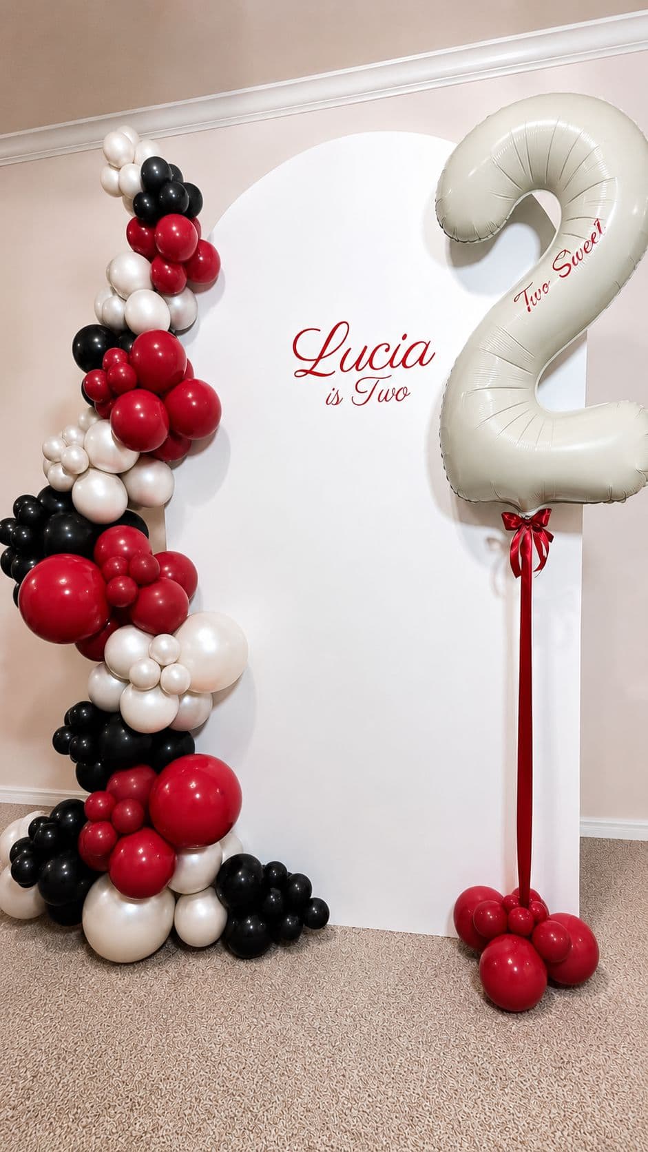 Red, black and white balloon garland on a white arch backdrop with a number 2 balloon for a second birthday