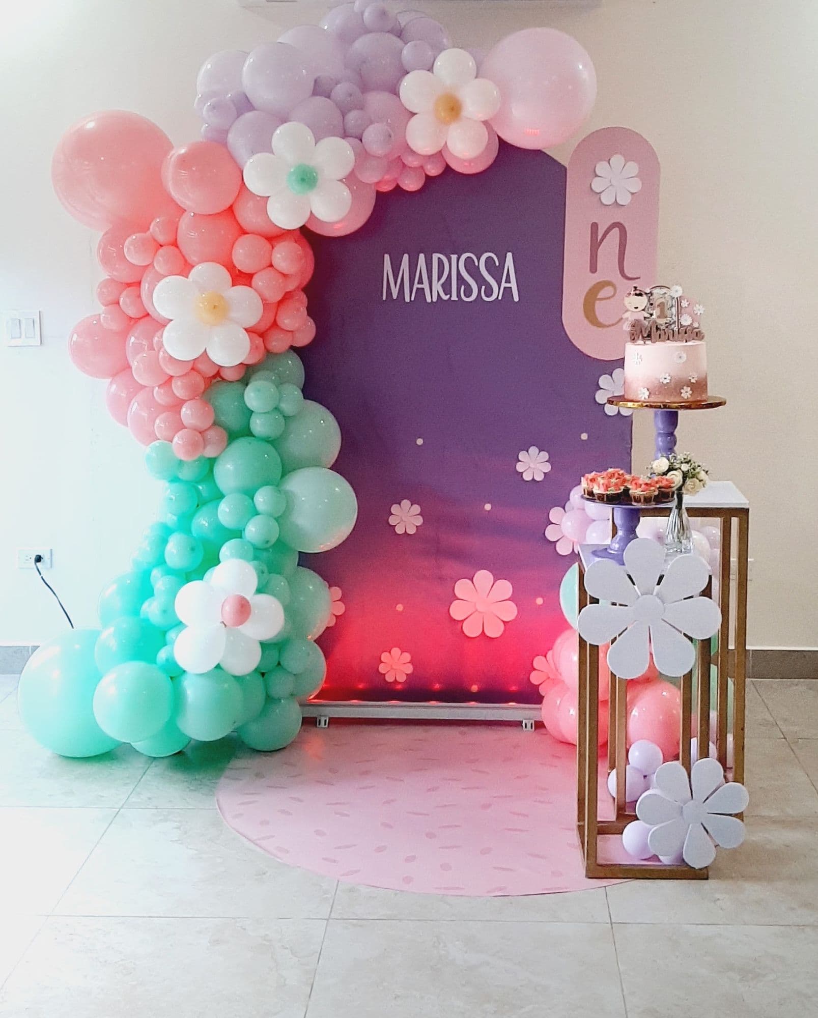 Pink and mint balloon garland with daisy accents on a purple backdrop for a groovy first birthday