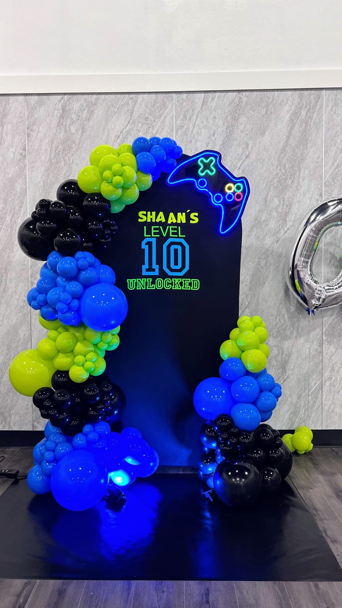 Blue, green and black balloon garland on a gamer-themed neon backdrop for a 10th birthday