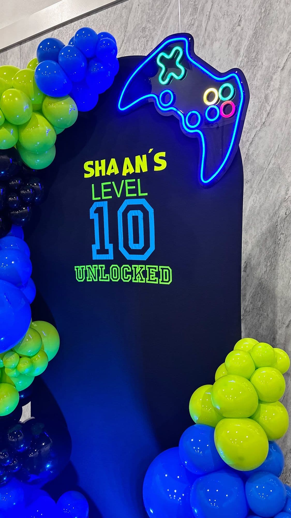 Close-up of the blue and green balloon garland and neon controller sign on a gamer birthday backdrop