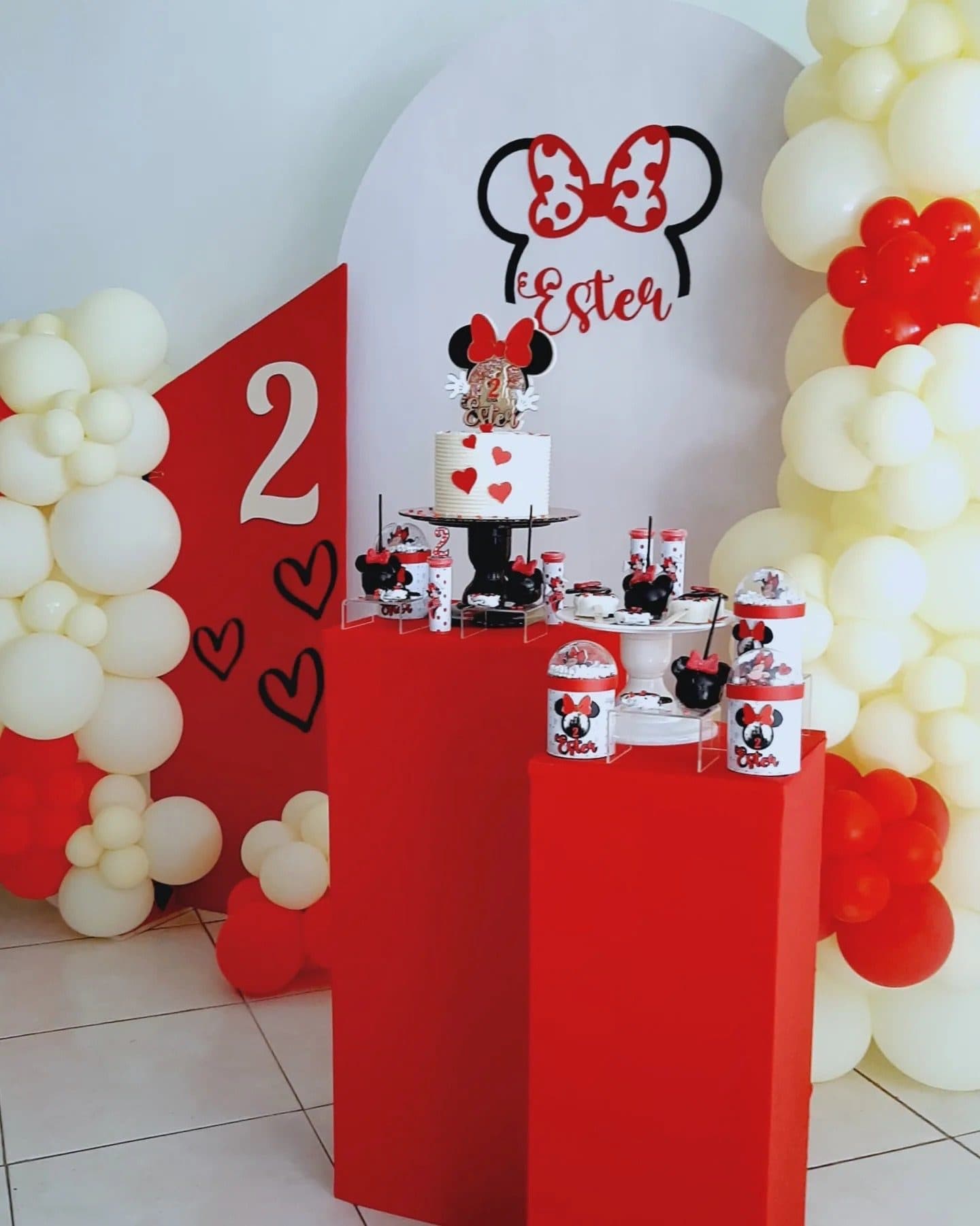 Wide view of a red, white and black Minnie Mouse themed second birthday dessert table with balloon columns
