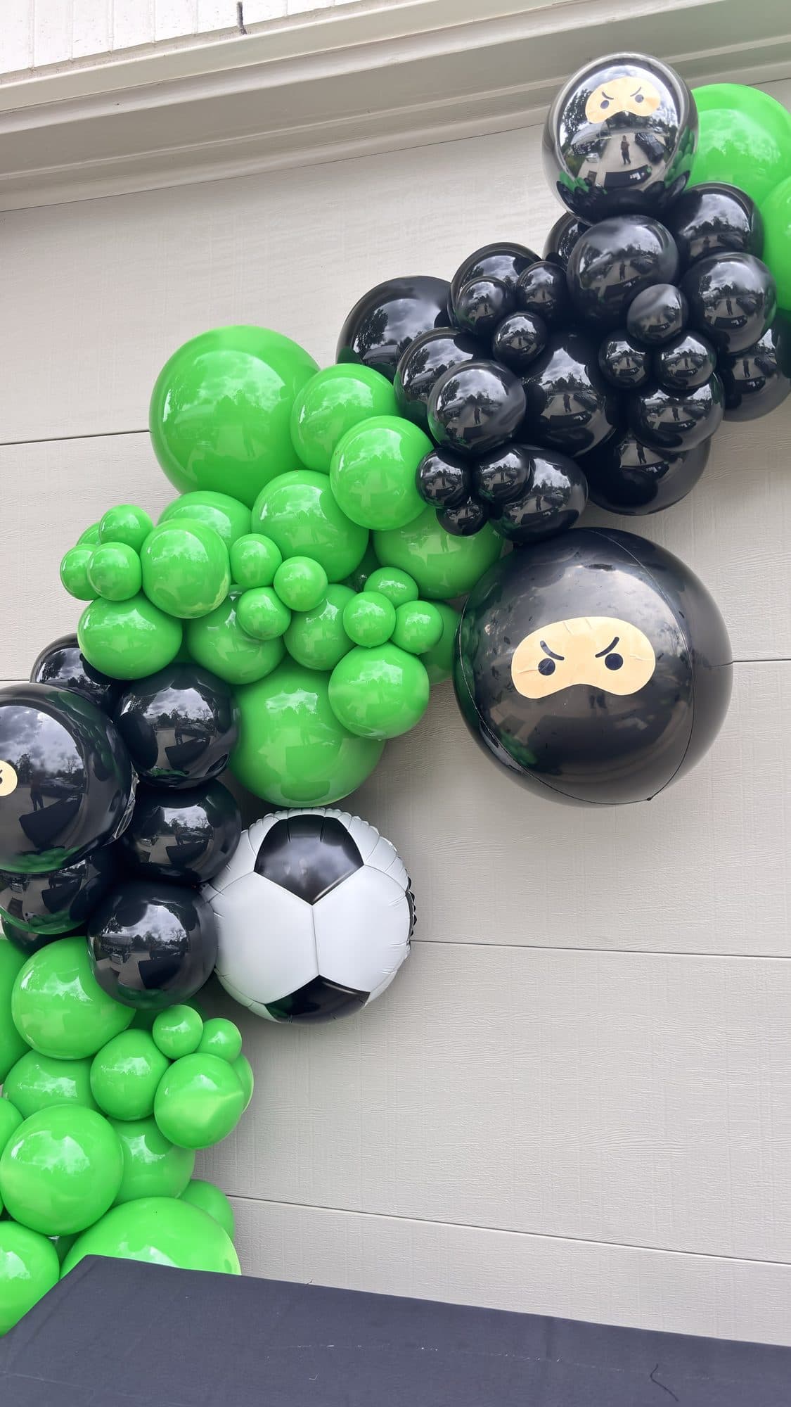 Green, black and white balloon garland with ninja and soccer ball balloons on a hallway wall