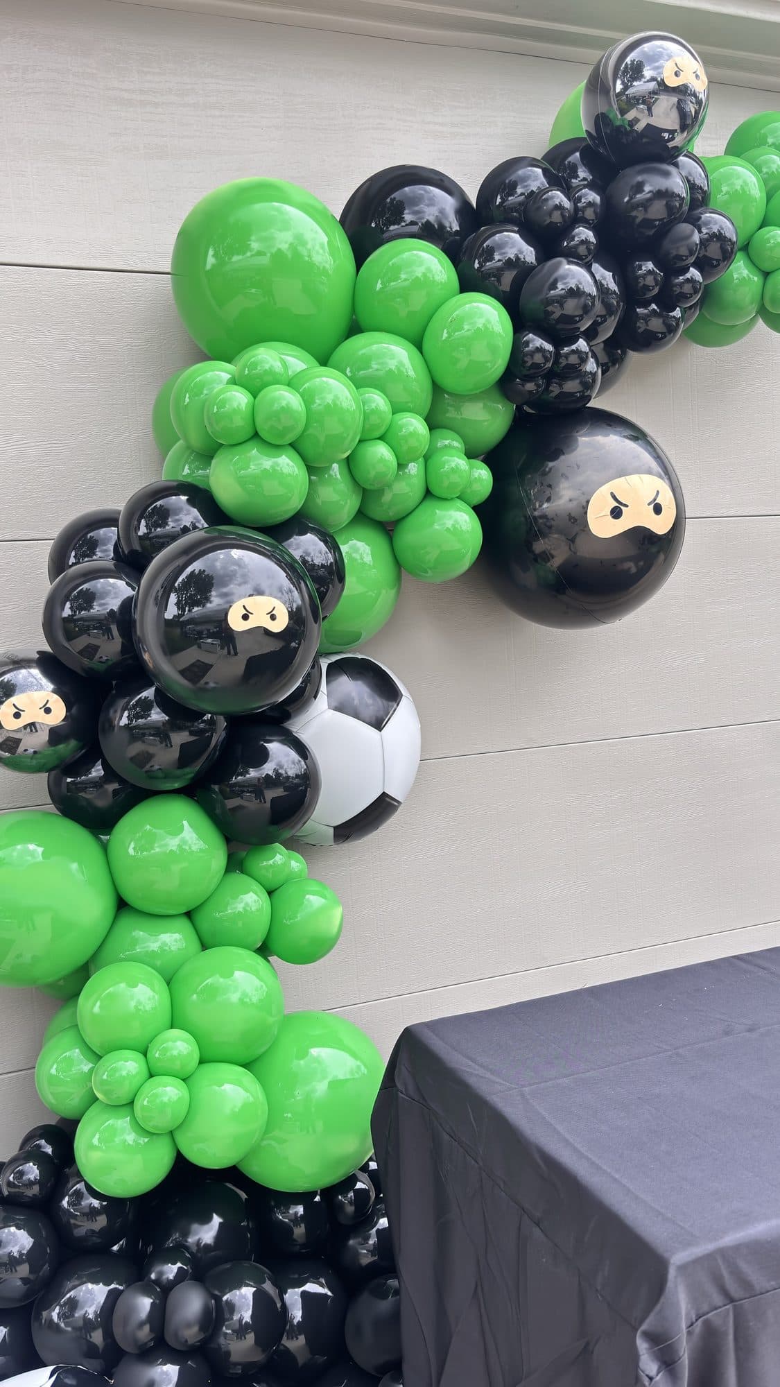 Wide view of a green, black and white ninja and soccer themed balloon garland in a gym hallway