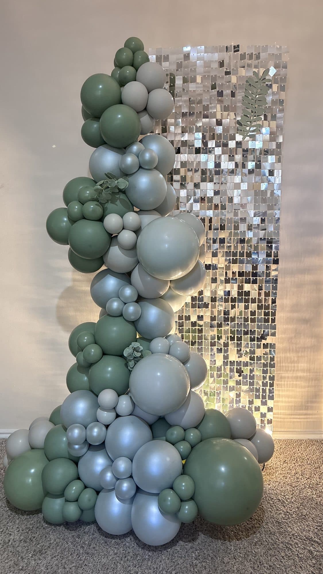 Sage green, cream and silver organic balloon column on a silver shimmer wall backdrop