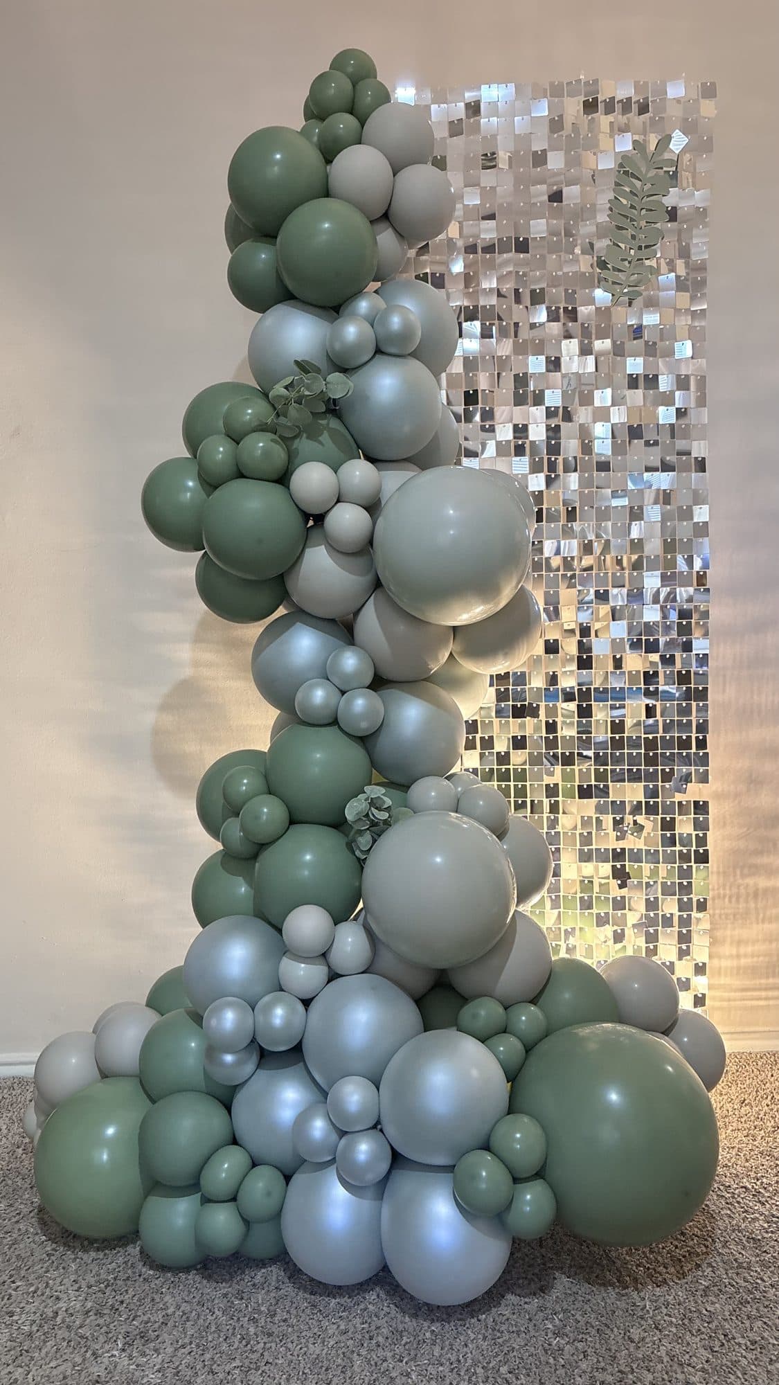 Close-up of the sage green, cream and silver organic balloon column on a shimmer wall backdrop