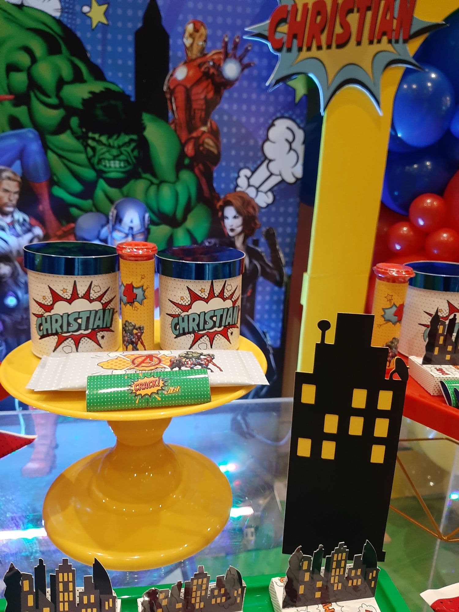 Superhero themed birthday dessert table with red, blue and yellow balloons and a comic backdrop