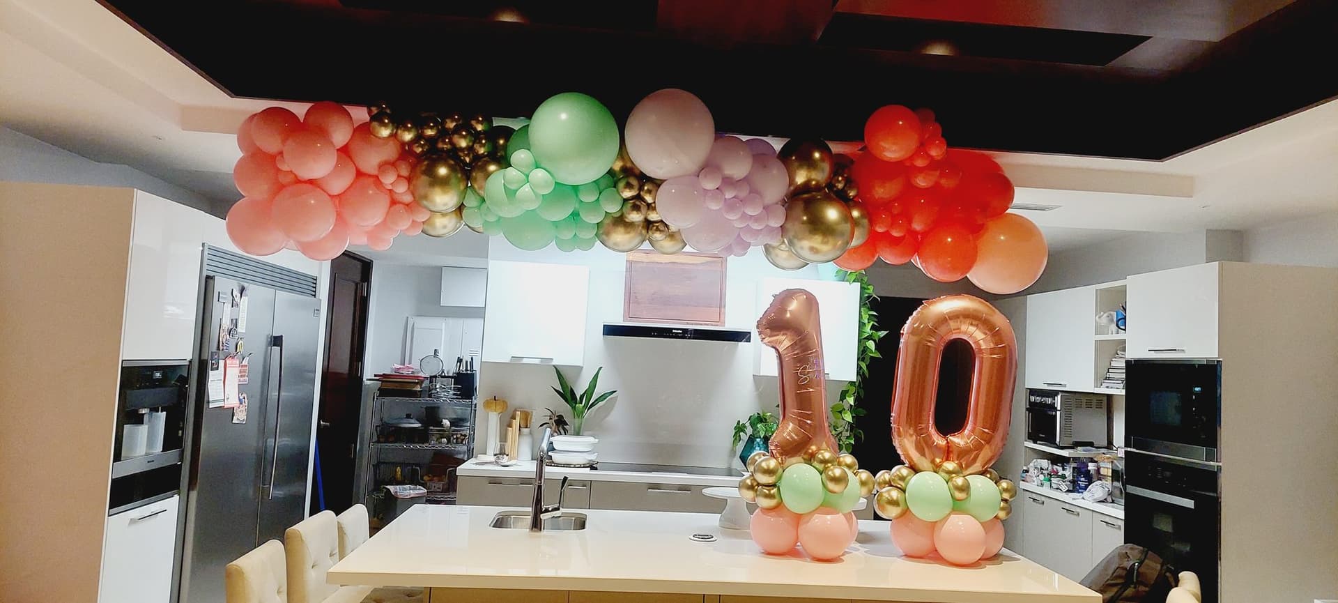 Orange, mint and red balloon garland over kitchen cabinets with number 10 balloons for a tenth birthday