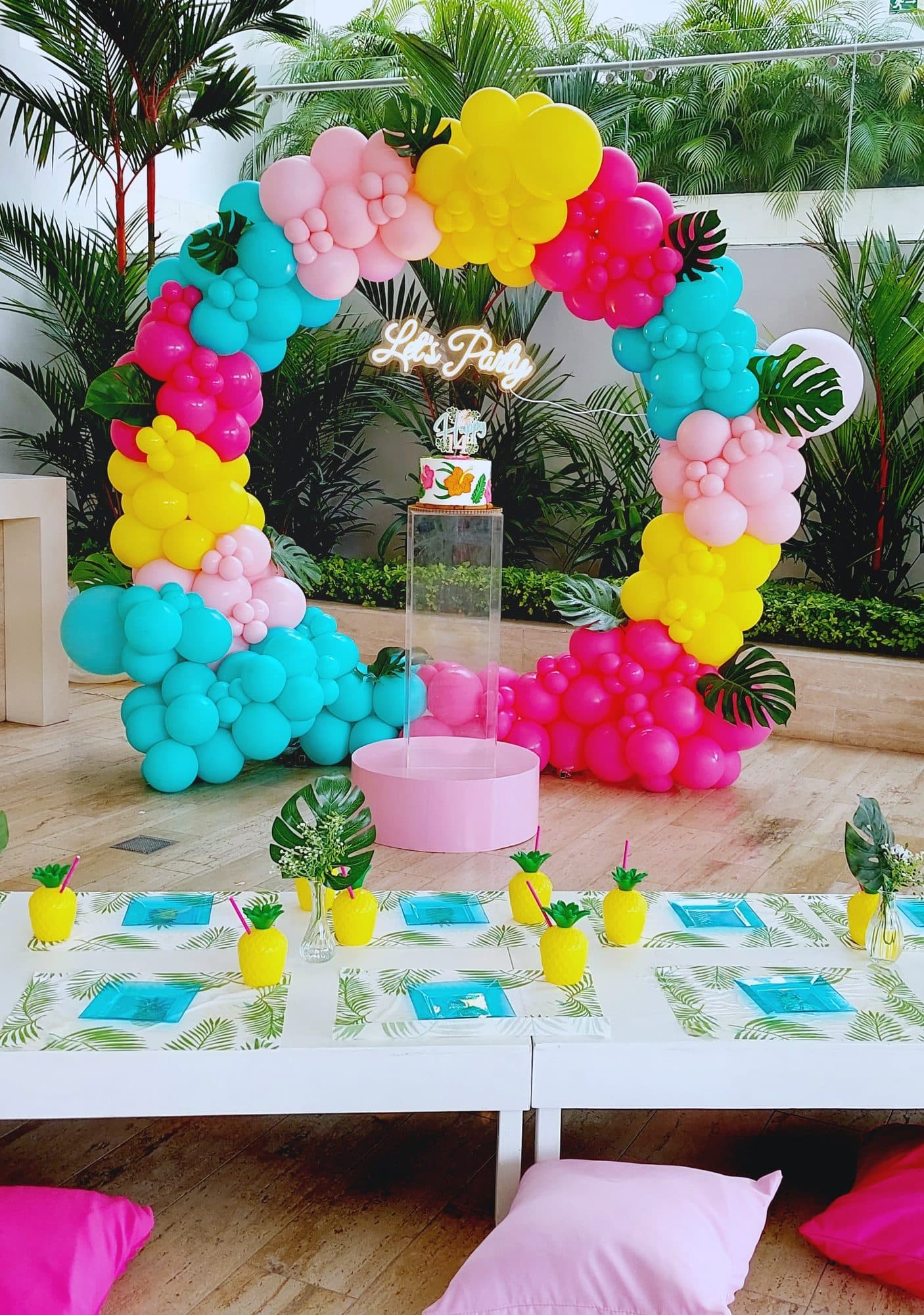 Pink, teal and yellow tropical balloon wreath arch over a party table with a Life's a Party neon sign