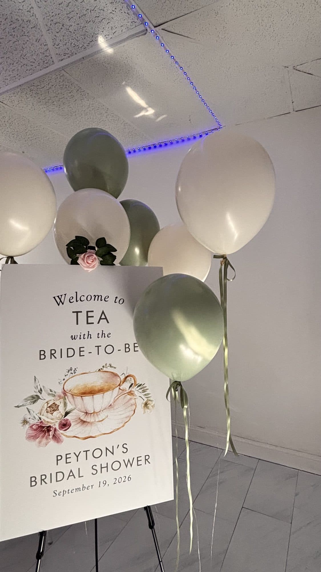 Bridal shower welcome sign on an easel beside cream and sage balloons