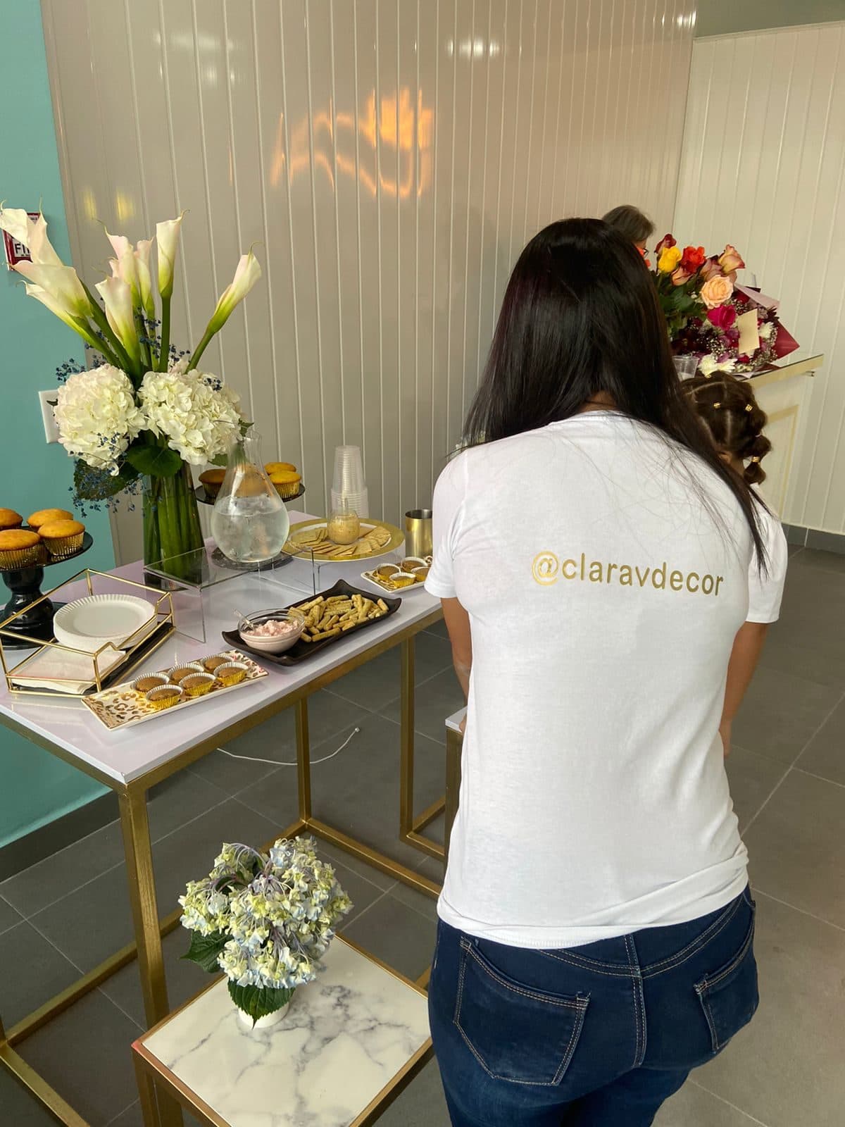 Clara Vento, wearing a ClaravDecor branded shirt, arranging a dessert table with flowers