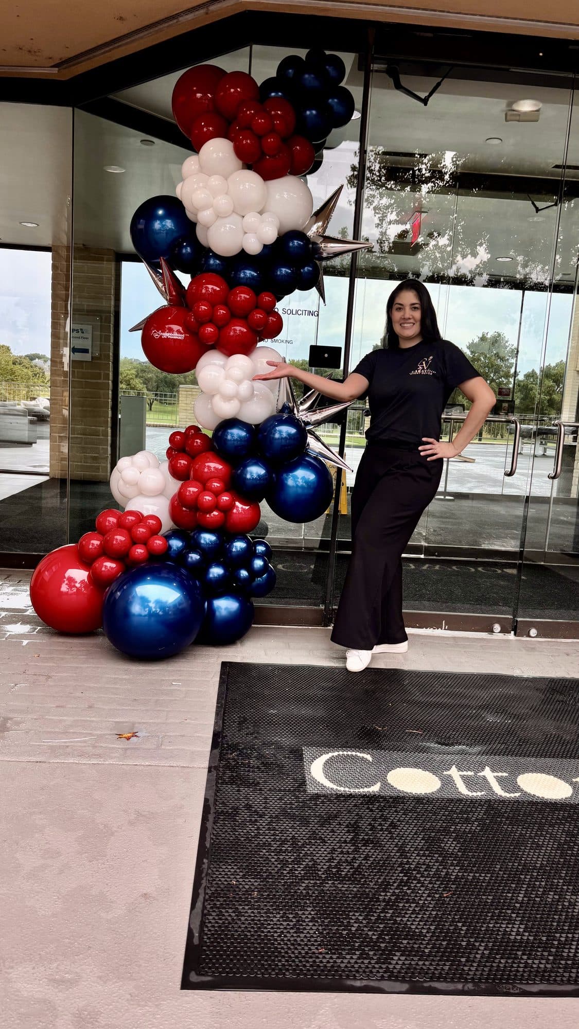 Clara Vento standing beside the navy, red and white balloon garland at the Neighborhood LTC Pharmacy office