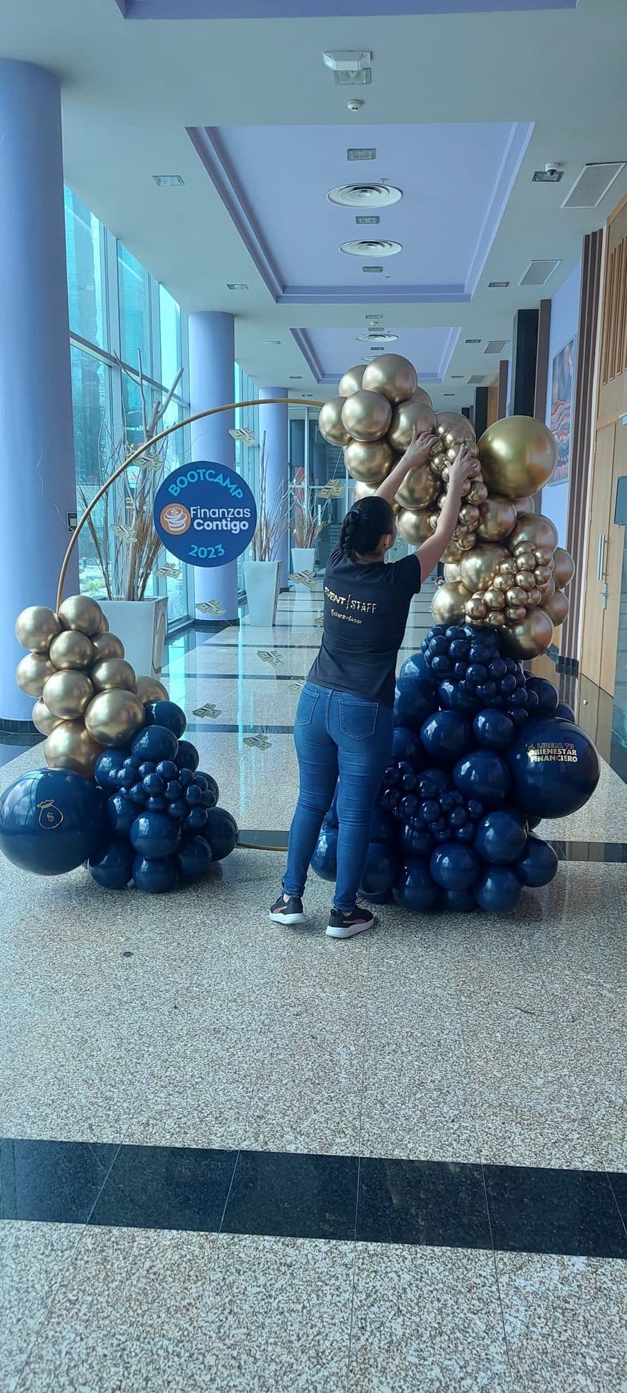 Navy, silver and gold balloon column being installed in a marble office lobby