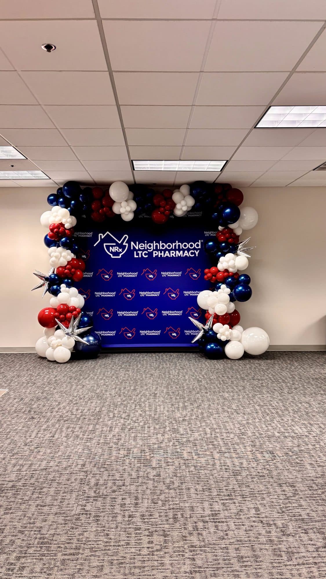 Navy, red and white balloon garland framing a Neighborhood LTC Pharmacy step-and-repeat backdrop