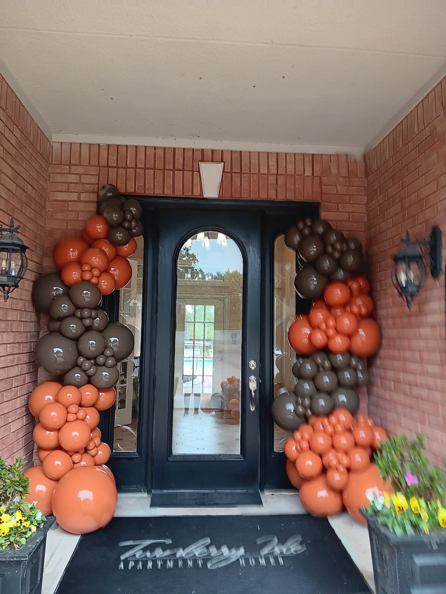 Orange, brown and black fall balloon garland flanking a brick front door entrance