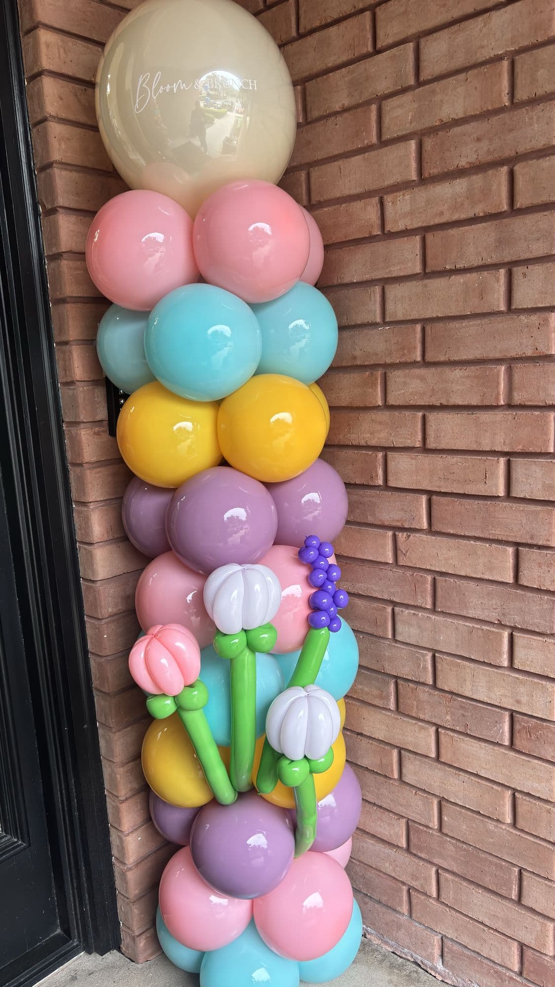 Pastel balloon column with tulip balloon accents beside a brick entryway for a spring celebration