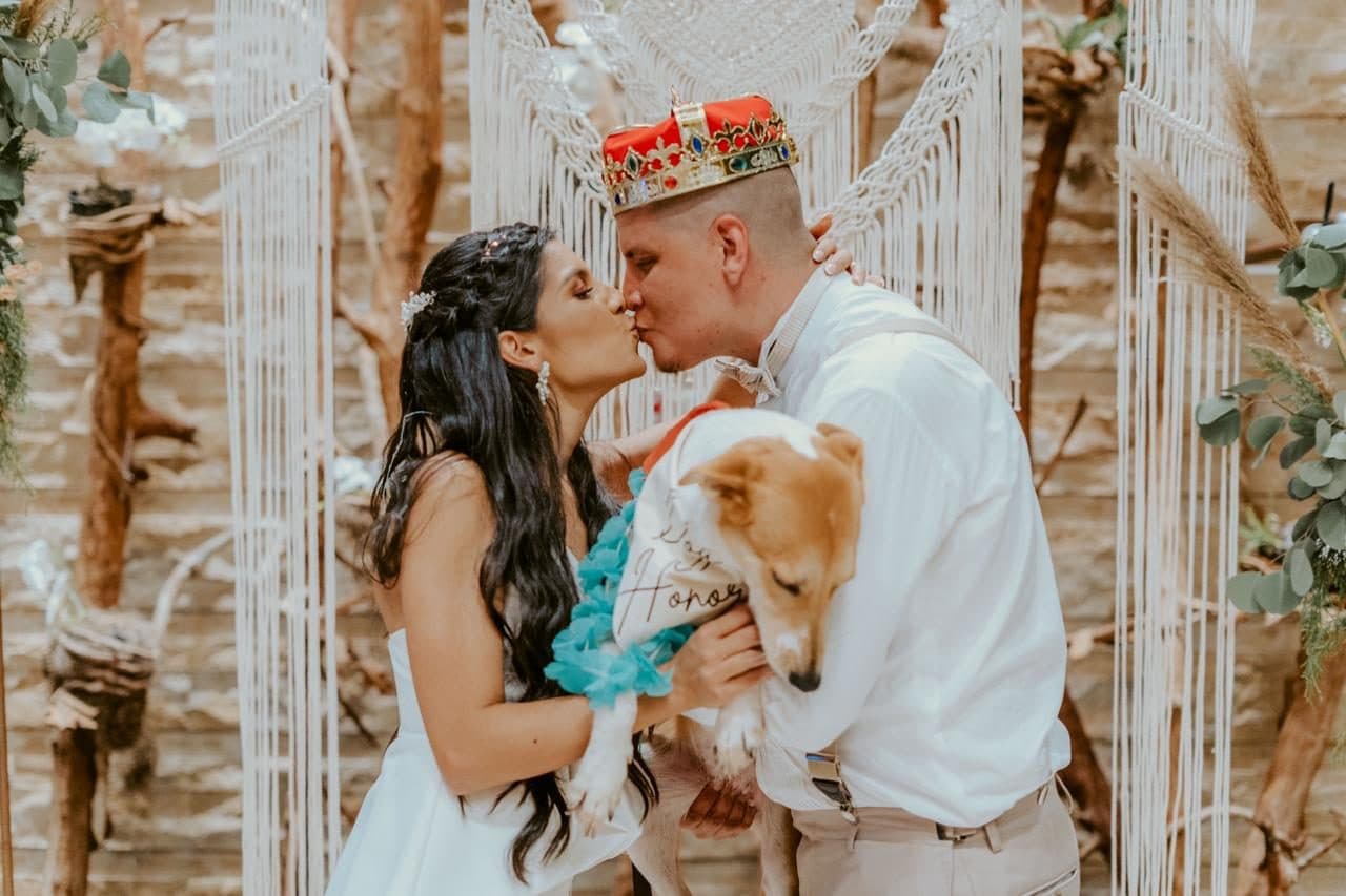 Close-up of the bride and groom kissing under the macrame ceremony arch with their dog