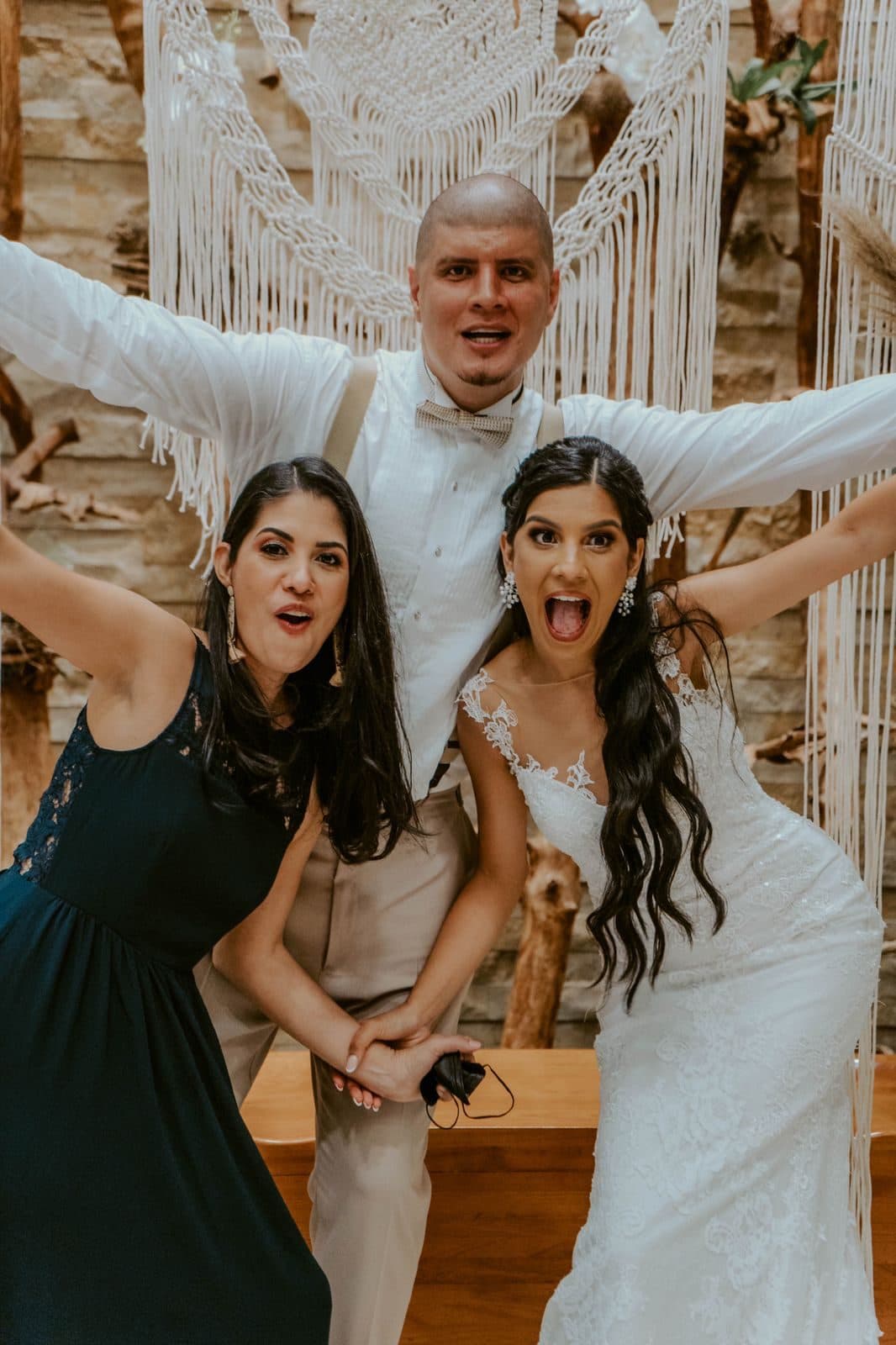 Wedding party posing in front of a macrame and driftwood photo wall with white floral accents